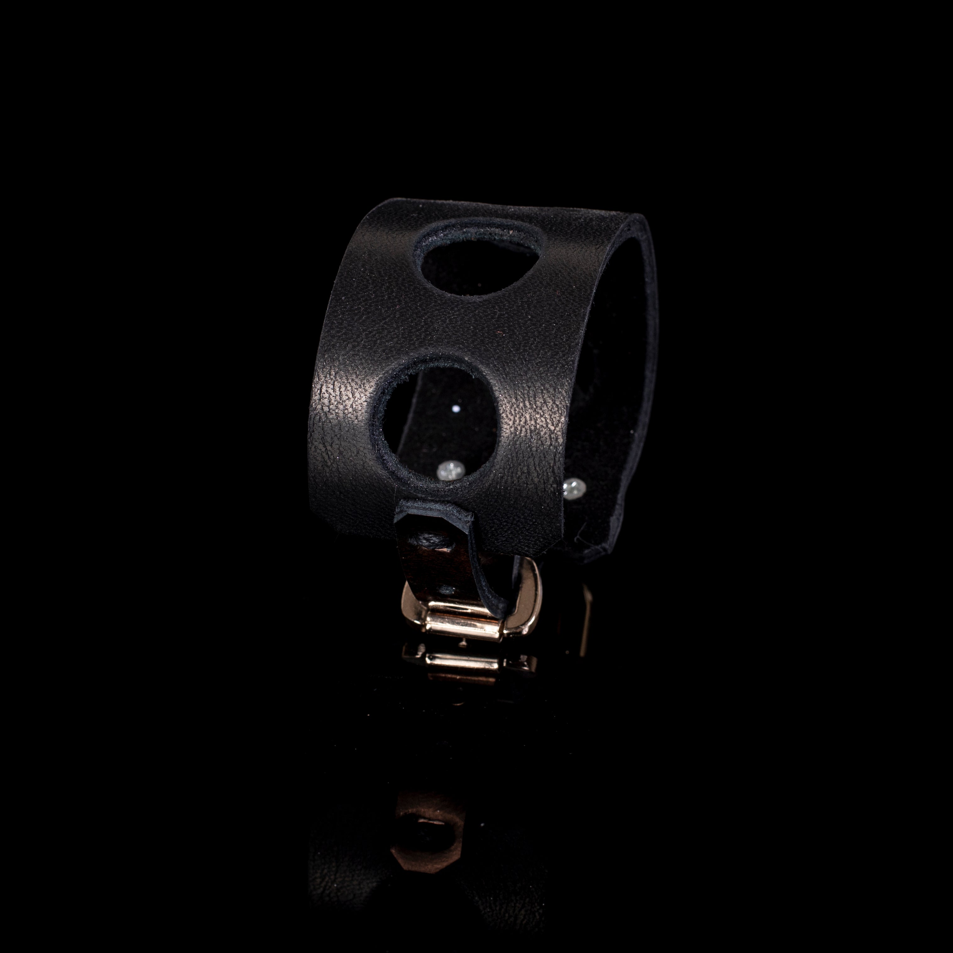 Wide black leather cuff bracelet with circular cutout design and gold buckle closure, minimalist handcrafted statement bracelet for women
