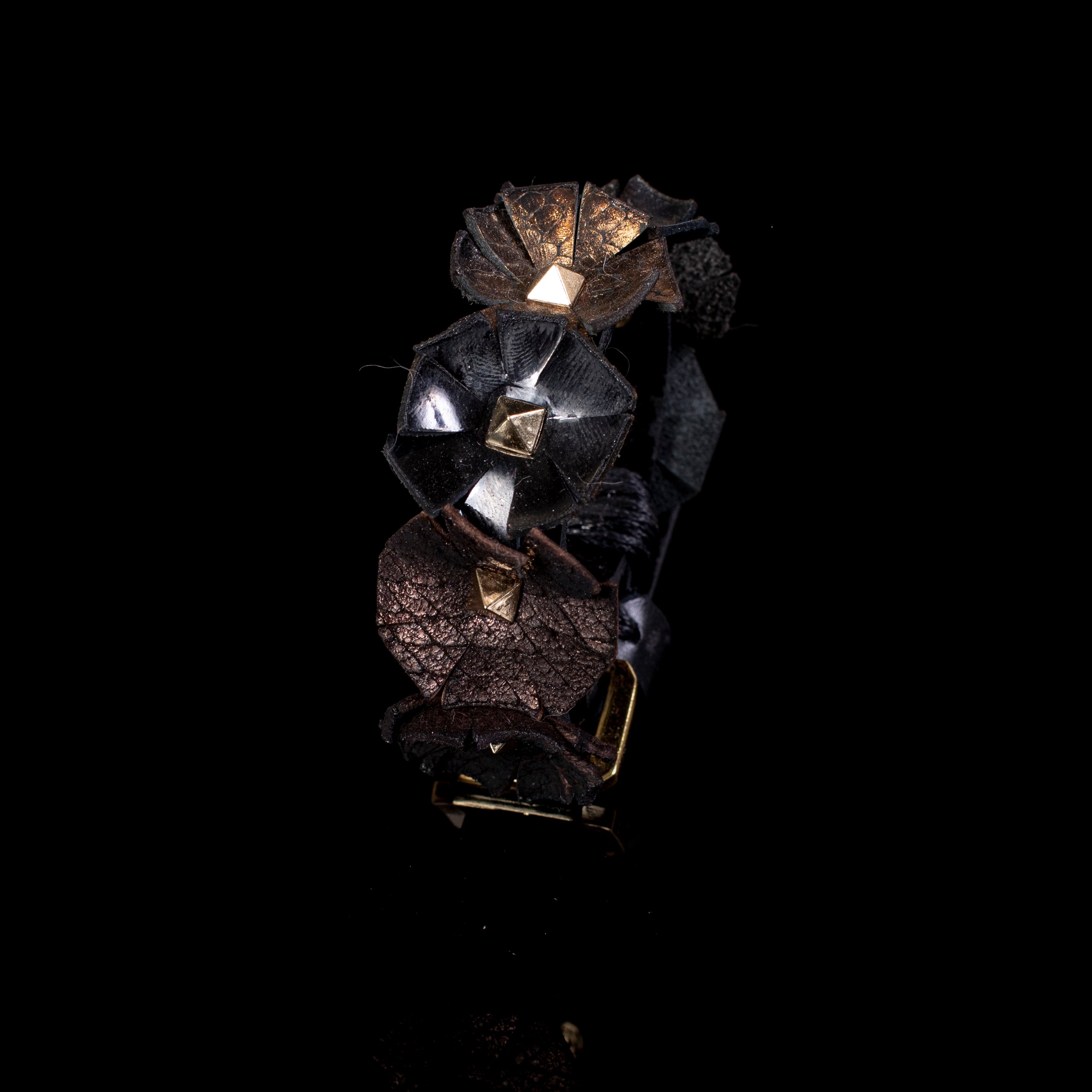 Black leather cuff with sculpted floral elements and gold pyramid studs