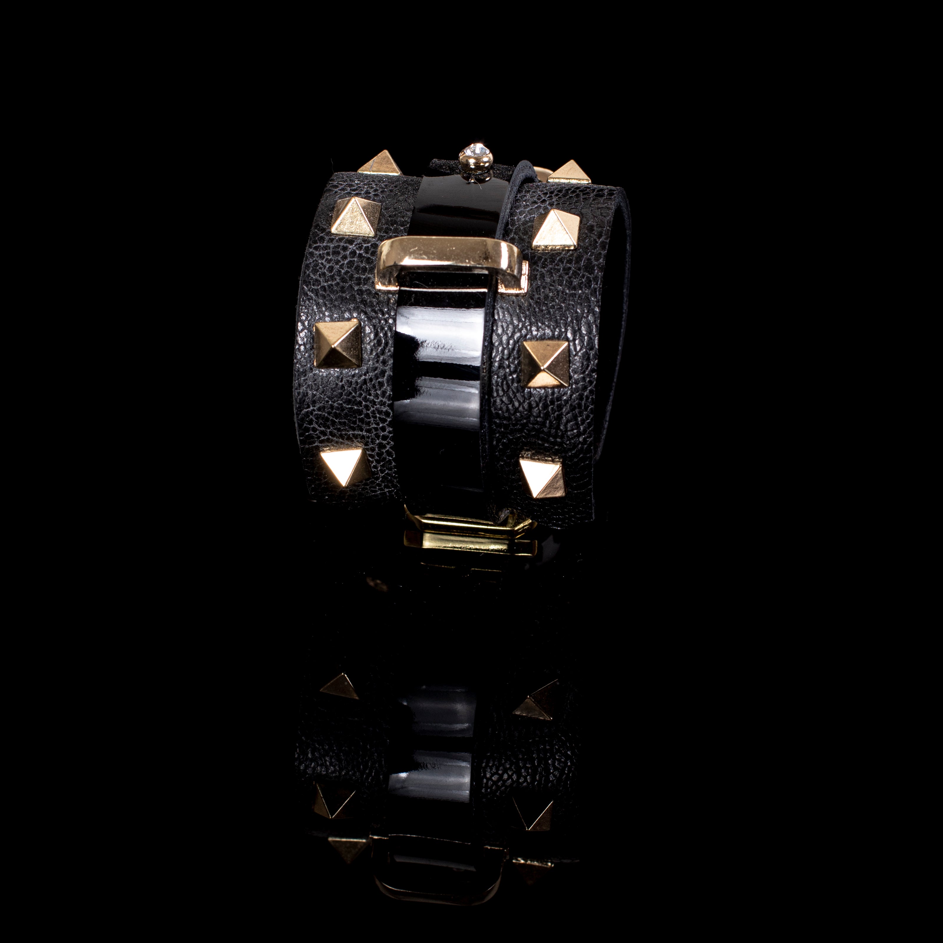 Black leather wrap cuff bracelet with gold pyramid studs, central glossy strip, crystal accent and gold buckle detail, handcrafted statement bracelet for women by THE DARK