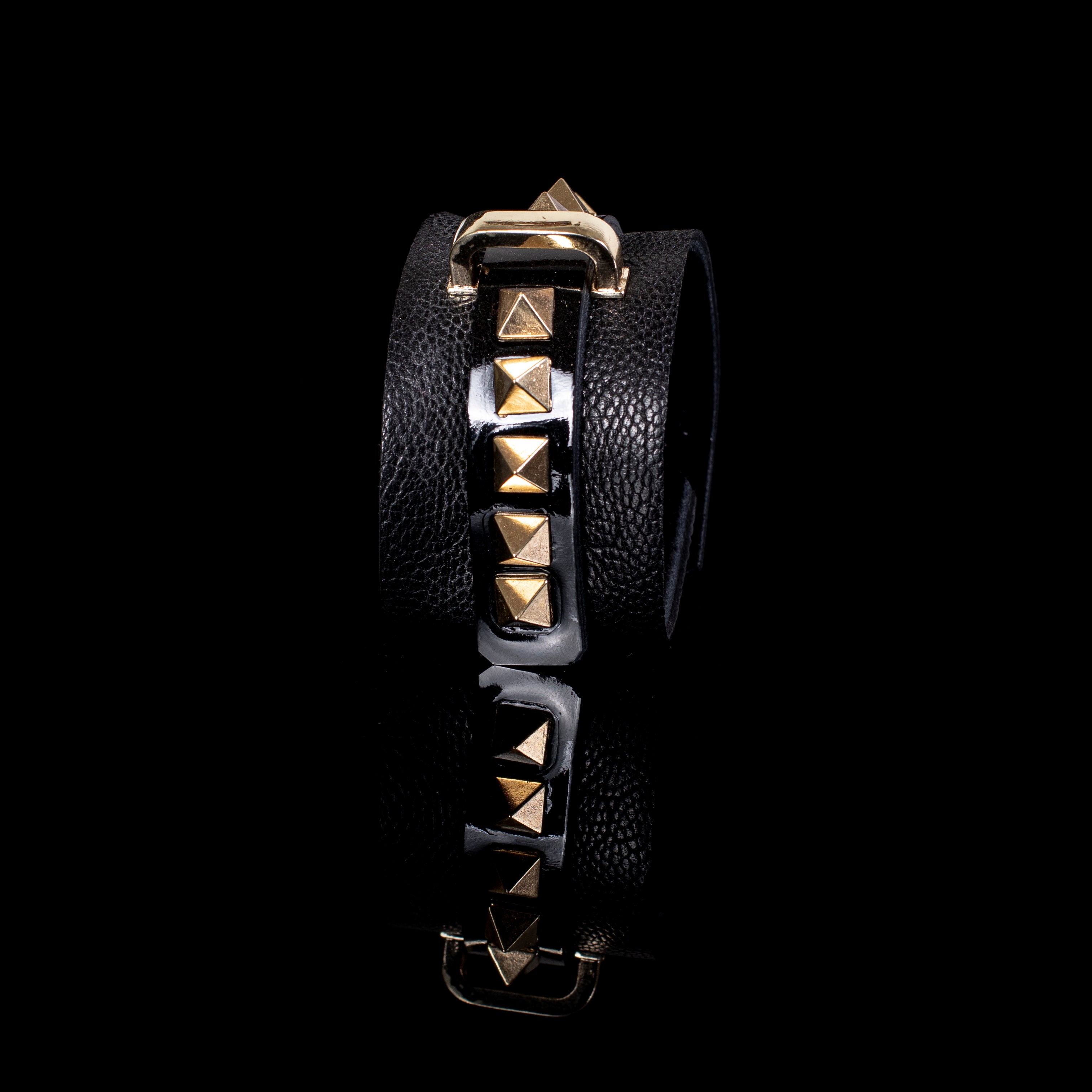 Black leather wrap cuff bracelet with gold pyramid studs, central glossy strip and gold buckle detail, handcrafted statement bracelet for women by THE DARK